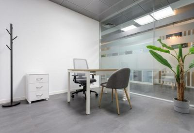 Private office suite with a minimal white desk, grey seating, and a potted plant.