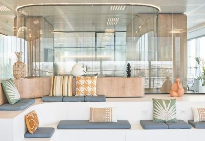 Modern communal area with tiered seating, colorful pillows, and glass-walled meeting rooms.