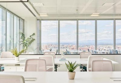 Bright open-plan office featuring white desks and chairs against large windows.