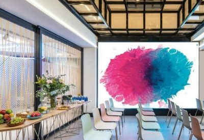 Spacious presentation room with rows of chairs and a large screen displaying colorful art.