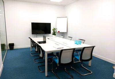 Meeting room with a white table, black chairs, and a large wall-mounted monitor.