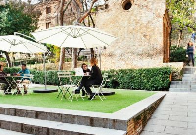 Outdoor communal terrace with umbrellas, artificial grass, and seating against a historic brick building.