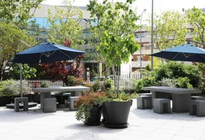 Outdoor terrace with stone tables, blue umbrellas, and potted greenery.