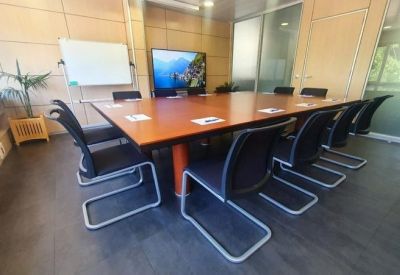 Large boardroom with a long wooden table, black cantilever chairs, and a display screen.