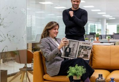 Two colleagues chatting on a leather sofa in a bright modern workspace.