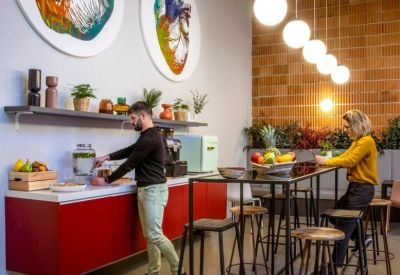 Modern office kitchen with red cabinets, circular artwork, and high-top seating.
