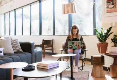Bright breakout space featuring a grey sofa, wooden coffee tables, and large windows.
