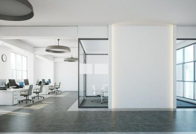 Open-plan office area with rows of white desks, ergonomic chairs, and modern pendant lighting.
