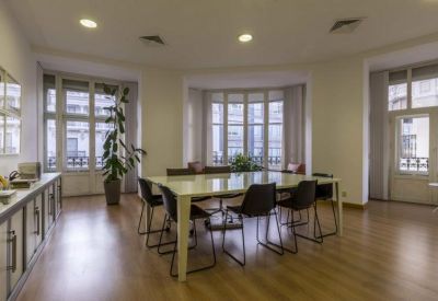 Bright boardroom with a large light-toned table, black chairs, and large bay windows.