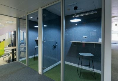 Private glass-enclosed phone booths with green carpeting and stools.