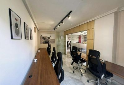 Long wooden coworking desk with several black chairs and minimalist wall art.
