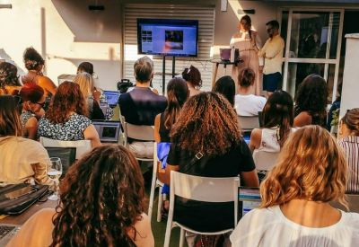 Outdoor presentation setting on a terrace with people seated in chairs facing a screen.