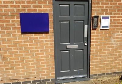 Close-up of the main entrance door with secure intercom system and blue signage.
