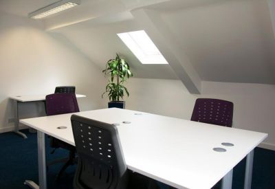 Bright shared workspace under a sloped ceiling with a skylight and indoor plant.