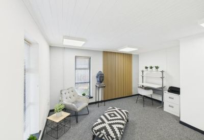 Professional private office with a patterned ottoman, grey armchair, and a minimalist workstation.