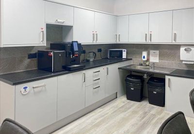 Clean communal kitchen area with white cabinetry and modern coffee machine.