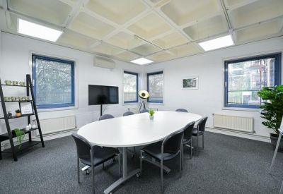 Professional meeting room featuring an oval white table, black chairs, and large windows.