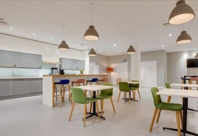 Vibrant communal kitchen and dining area with green chairs and pendant lighting.