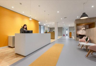 Reception lobby with a white desk, yellow feature wall, and comfortable lounge seating.
