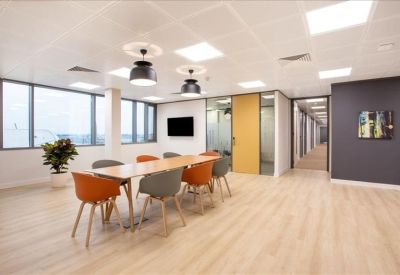 Bright breakout space with light wood floors and colorful orange and grey seating.