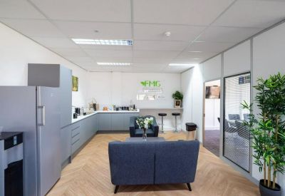 Modern communal kitchen and lounge area with wood-effect flooring and blue sofas.