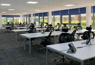 Large open-plan office with rows of white desks and black ergonomic chairs.