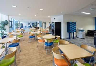 Spacious dining area with wooden tables and vibrant blue, orange, and green chairs.