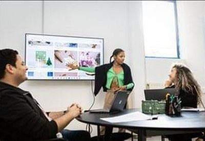 Meeting room with a large wall-mounted screen showing a presentation and people at a table.