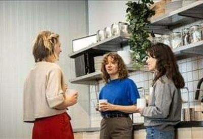 Coworkers talking in a modern kitchen area with open shelving and potted plants.