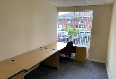 Private office suite featuring a wooden corner desk and a window with vertical blinds.