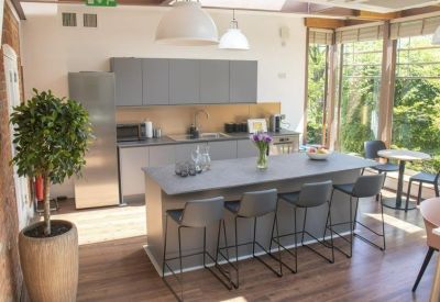 Modern communal kitchen and breakout area with a grey island, breakfast bar, and large windows.