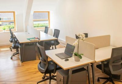 Sunlit open-plan office with white desks, ergonomic chairs, and large windows.