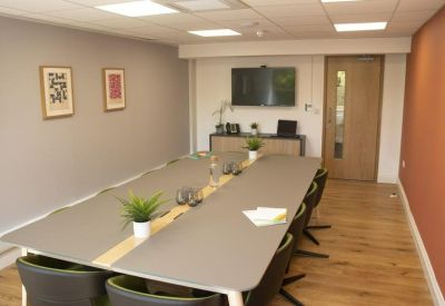 Professional meeting room featuring a long grey conference table and wall-mounted screen.