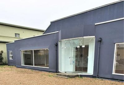 Glass entrance doors leading into a modern blue building with gravel forecourt.