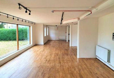 Spacious open-plan workspace featuring warm wood-laminate flooring and large windows.