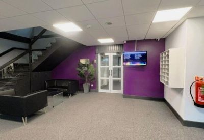 Modern building reception area featuring a purple feature wall, black leather sofas, and a wall-mounted screen.
