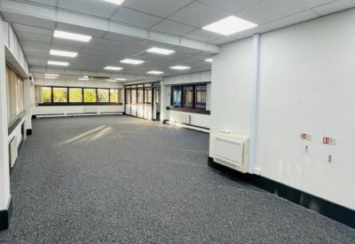 Spacious open-plan office with grey carpeting, white walls, and bright overhead LED panel lighting.