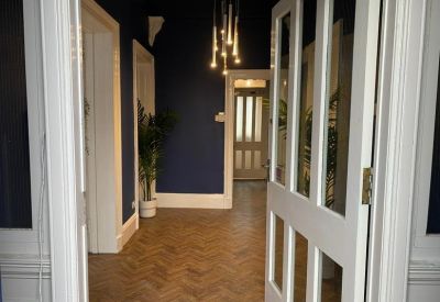 Grand entrance hallway with dark blue walls, herringbone wood flooring, and a modern chandelier.