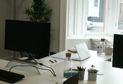 Shared workspace with white desks, computer monitors, and potted plants.