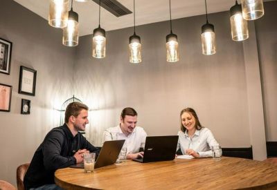Three people working on laptops at a wooden table under industrial pendant lighting.