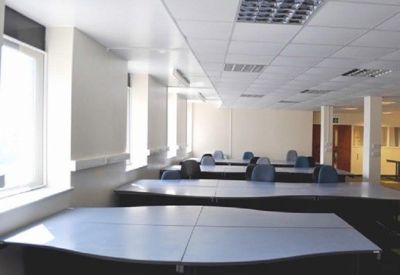 Bright open-plan office space with rows of curved blue desks and overhead grid lighting.