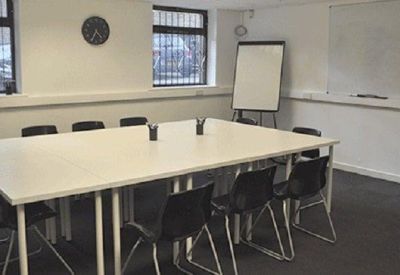 Spacious meeting room with a large white table, black chairs, and a whiteboard.