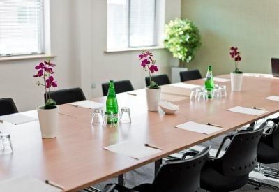 Formal boardroom with long wooden table, leather chairs, and floral arrangements.