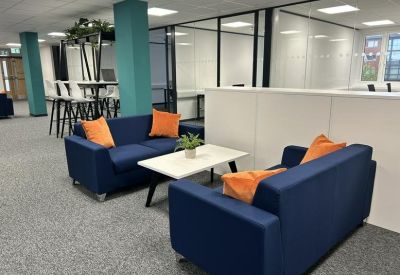 Lounge area with navy sofas and bright orange cushions in an open-plan office.