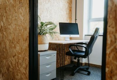Private office space featuring a desk with a monitor, black chair, and a potted plant.