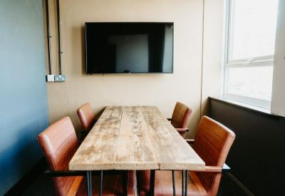 Meeting room with a large wooden table, brown leather chairs, and a wall-mounted TV.