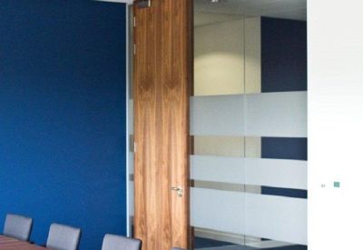 Modern boardroom featuring a large wood-finish table and glass partitioning.