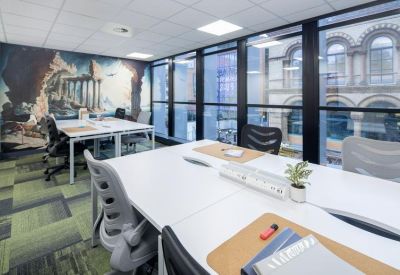 Collaborative workspace with white desks, greenery, and a classical architecture wall mural.