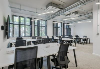 Bright open-plan office with white desks, ergonomic black chairs, and large windows.