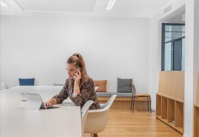 Woman in a leopard print jacket working on a tablet in a bright, modern meeting room.